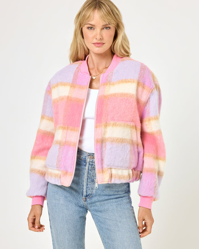 Close-up front view of a model wearing the LSPACE Quinn Jacket in point dume plaid, featuring a soft fuzzy plaid pattern in pink, lavender, and cream with a zip-up bomber silhouette and ribbed cuffs.
