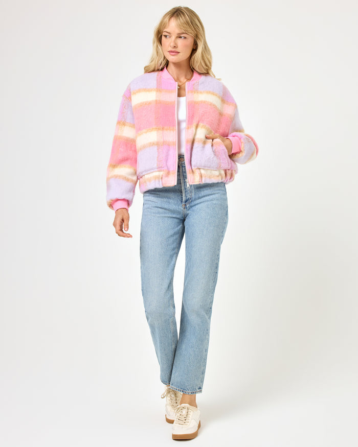 Front view of a model wearing the LSPACE Quinn Jacket in point dume plaid, a cozy oversized bomber jacket with a pink, lavender, and cream plaid pattern, styled with wide-leg jeans and sneakers.
