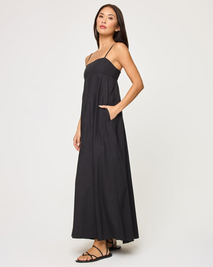 Side view of a model wearing the LSPACE Raveena Dress in black, showing the relaxed A-line silhouette of the maxi dress with a visible side pocket.
