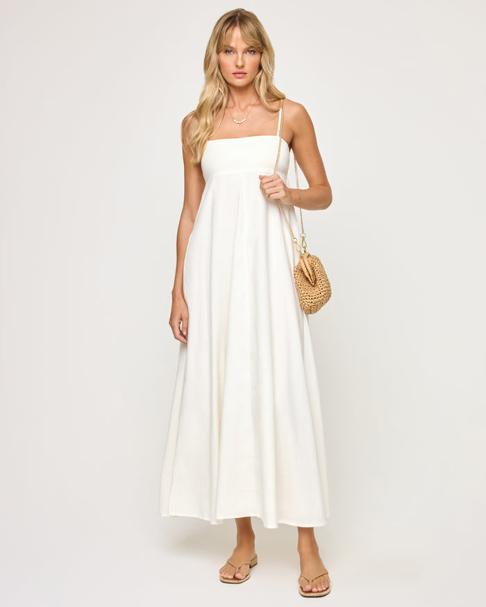Front view of a model wearing the LSPACE Raveena Dress in cream, a relaxed A-line maxi dress with a square neckline and thin spaghetti straps, styled with a small woven bag.