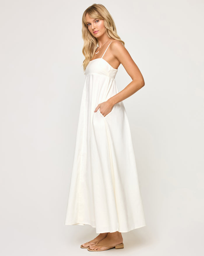 Side view of a model wearing the LSPACE Raveena Dress in cream, showing the relaxed A-line silhouette with a fitted square bodice and a full flowing maxi skirt with a side pocket.