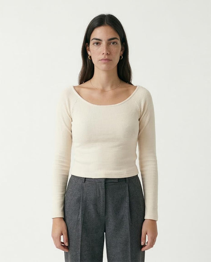 Woman wearing a beige long-sleeve top and gray pants on a white background