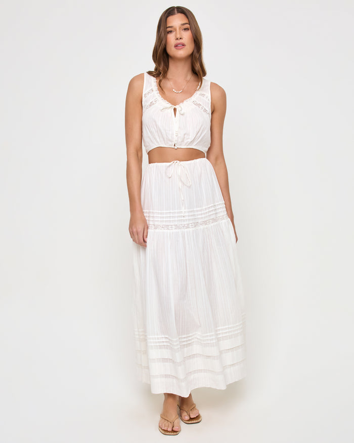 Front view of a model wearing the LSPACE Reia Skirt in white, a tiered maxi skirt with pin-tuck and lace trim details, styled with the matching Reia top, on a white studio background.
