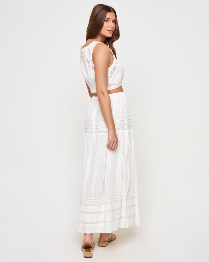Three-quarter back view of a model wearing the LSPACE Reia Skirt in white, showing the back of the tiered maxi skirt with lace trim detail, styled with the matching Reia top, on a white studio background.