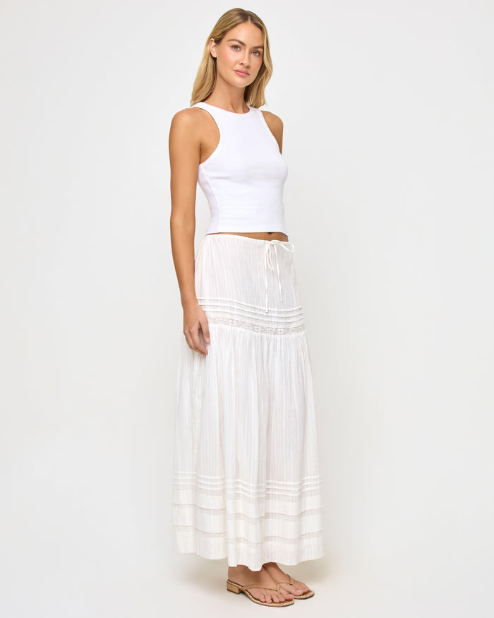 Three-quarter front view of a model wearing the LSPACE Reia Skirt in white, a tiered maxi skirt with pin-tuck and lace trim details, styled with a white crop top, on a white studio background.