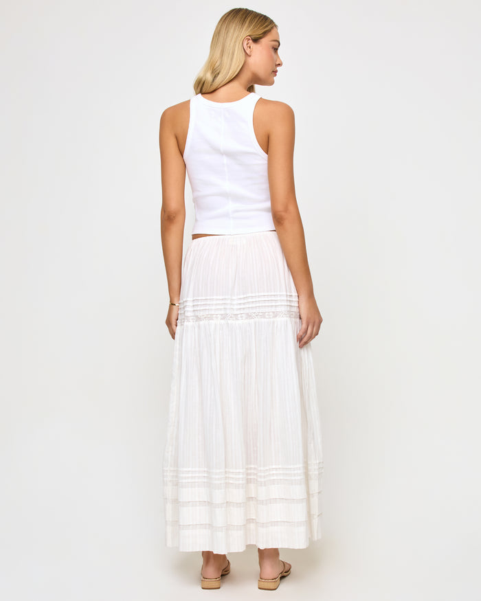 Back view of a model wearing the LSPACE Reia Skirt in white, showing the back of the tiered maxi skirt with pin-tuck and lace trim detail, styled with a white crop top, on a white studio background.