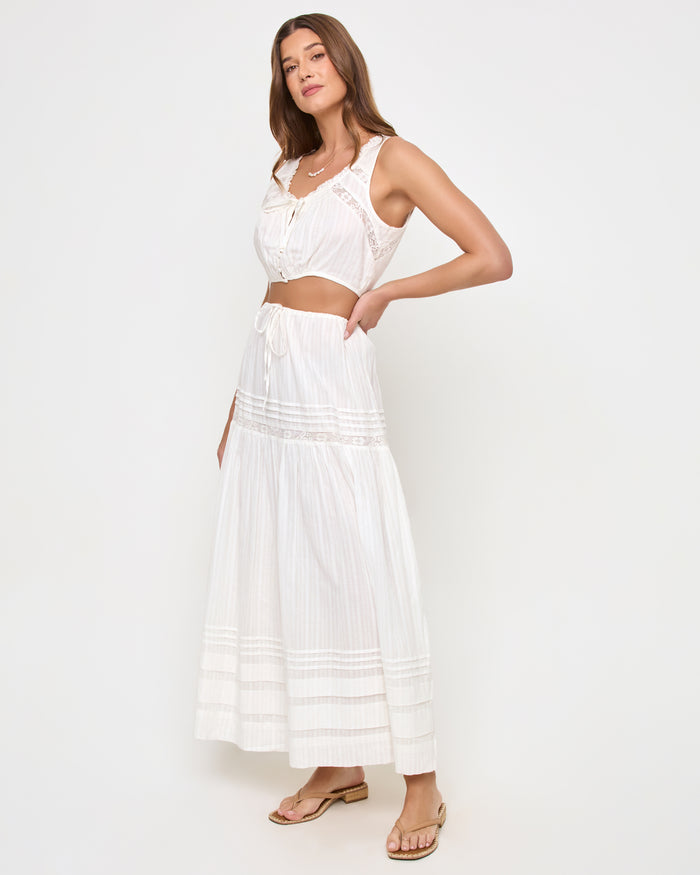 Three-quarter view of a model wearing the LSPACE Reia Top in white, a sleeveless tie-front crop top with lace trim, styled with the matching white tiered maxi skirt, on a white studio background.