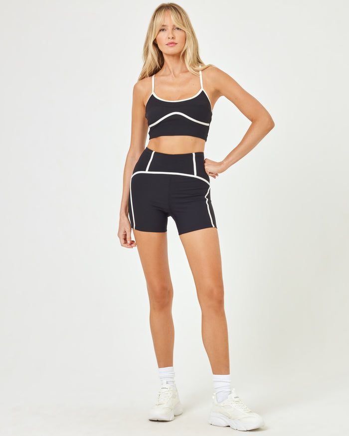 Front view of model wearing the Revel Top in black-cream with matching black-cream Revel Short and white sneakers.