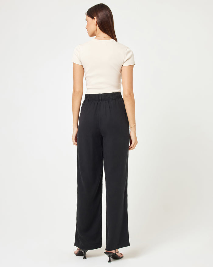 Back view of a model wearing the LSPACE Rhodes Pant in black, showing the wide-leg silhouette and elasticated back waistband, styled with a white crop top and strappy heels.