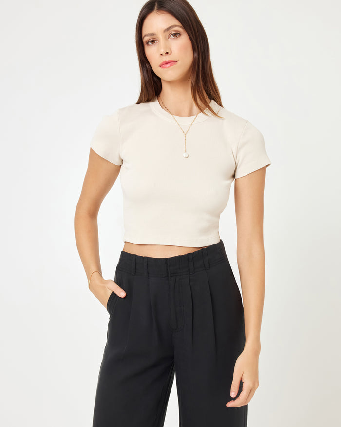 Close-up front view of a model wearing the LSPACE Rhodes Pant in black, highlighting the pleated high-rise waistband and wide-leg cut, styled with a white crop top.