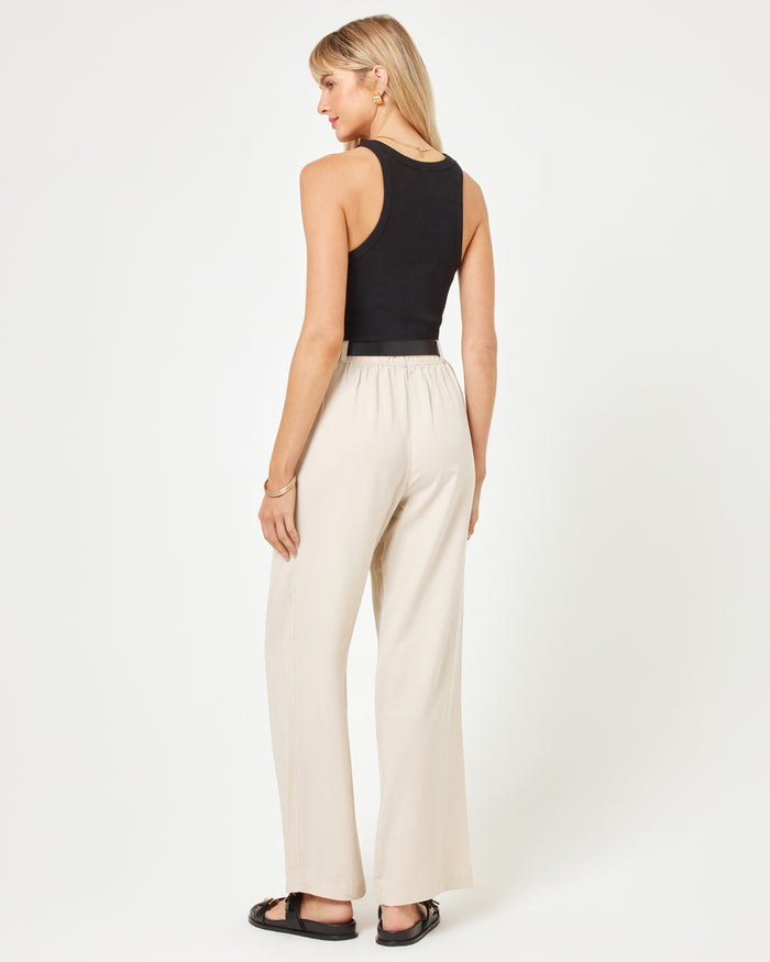 Back view of a model wearing the LSPACE Rhodes Pant in oyster, showing the elasticated back waistband and wide-leg silhouette, styled with a black tank top and sandals.