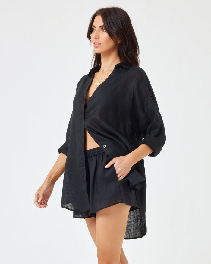 Side view of a model wearing the open LSPACE Rio Tunic in black over matching black linen shorts.