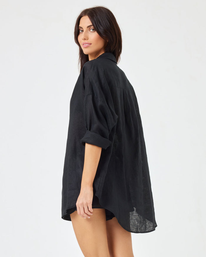 Back angled view of a model wearing the LSPACE Rio Tunic in black over matching black linen shorts.