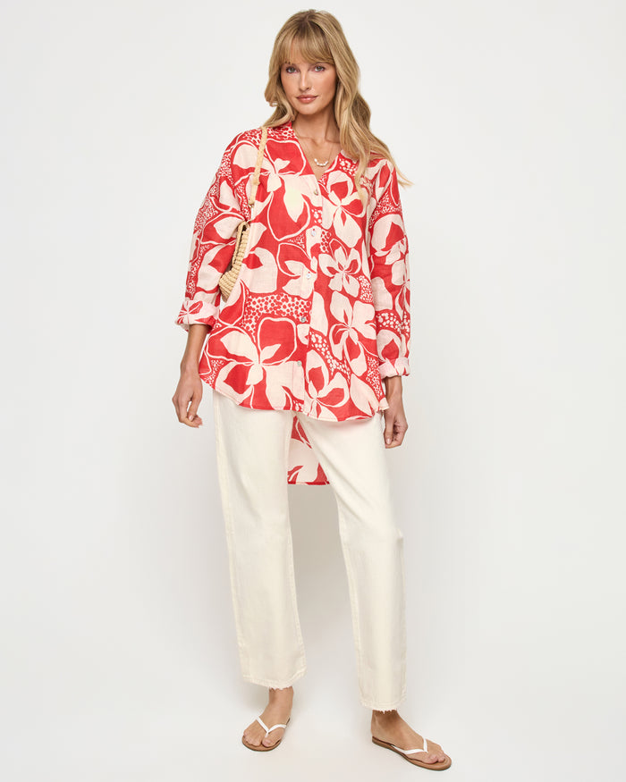 Front view of a model wearing the LSPACE Rio Tunic in hibiscus bloom styled over white wide-leg pants, demonstrating the tunic's versatility as a beach cover-up with 3/4 sleeves and bold hibiscus print.