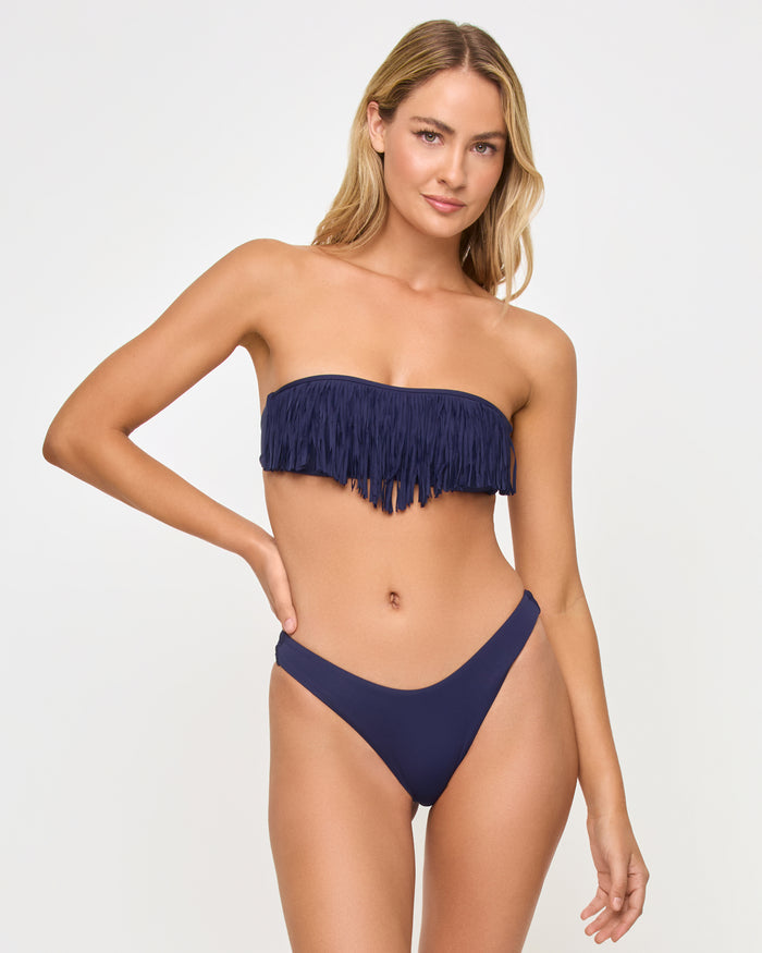 Front view of a model wearing the LSPACE Rocky Bikini Bottom in Sensual Solid Midnight Blue navy with a high-cut leg, paired with a navy fringe bandeau Dixie Bikini Top.