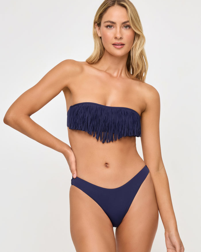 Close-up front view of a model wearing the LSPACE Rocky Bikini Bottom in Sensual Solid Midnight Blue navy with a high-cut leg opening, paired with a navy fringe bandeau Dixie Bikini Top..