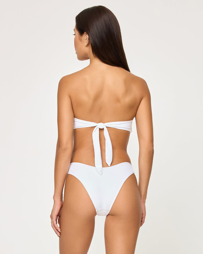 Back view of a model wearing the LSPACE white Rocky Bikini Bottom, a cheeky low-rise style, paired with a matching white fringe strapless Dixie Bikini Top, showing the back tie closure.