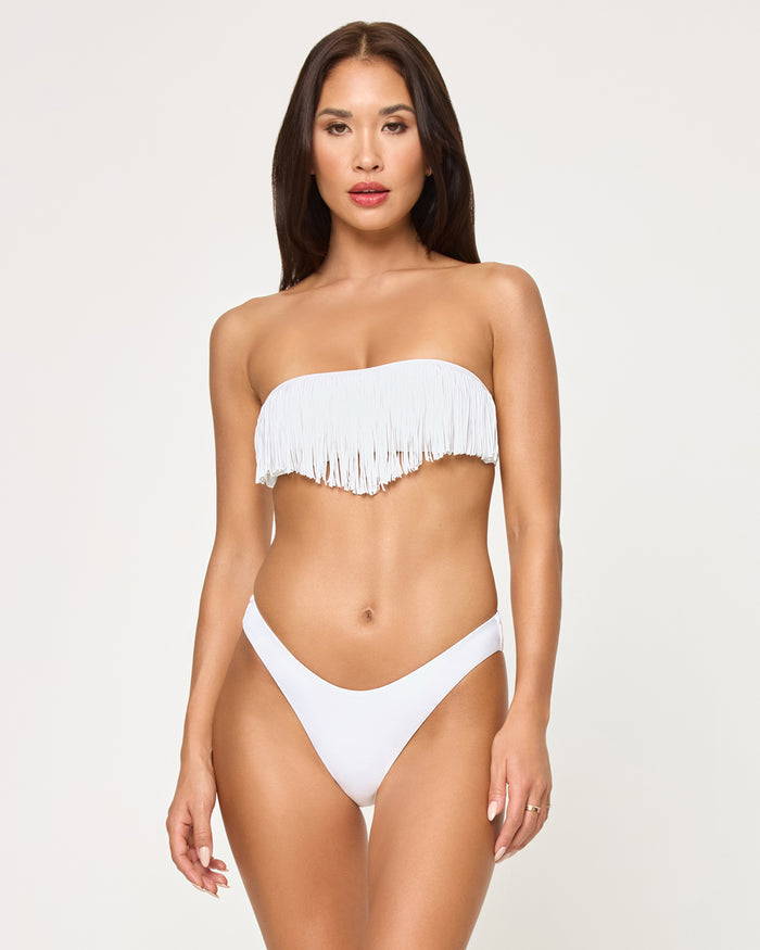 Front view of a model wearing the LSPACE white Rocky Bikini Bottom, a cheeky low-rise style, paired with a matching white fringe strapless Dixie Bikini Top.
