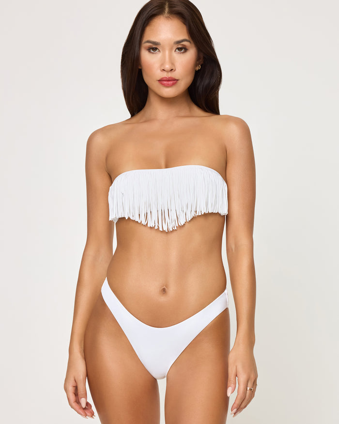 Front view of a model wearing the LSPACE white Rocky Bikini Bottom, a cheeky low-rise silhouette in solid white fabric, paired with a matching white fringe strapless Dixie Bikini Top.