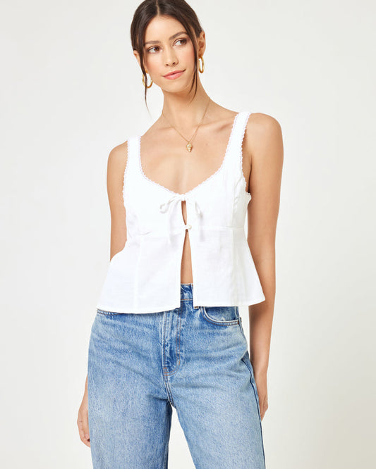 Close-up front view of a model wearing the LSPACE Rosa Top in cream, featuring a scoop neckline with tie-front detail, frayed strap trim, and a flared peplum hem, styled with blue jeans.