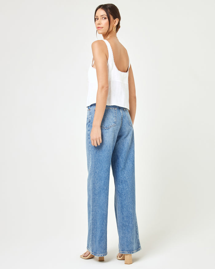 Back view of a model wearing the LSPACE Rosa Top in cream, showing the low open back and scoop back neckline with frayed strap trim, styled with wide-leg blue jeans.