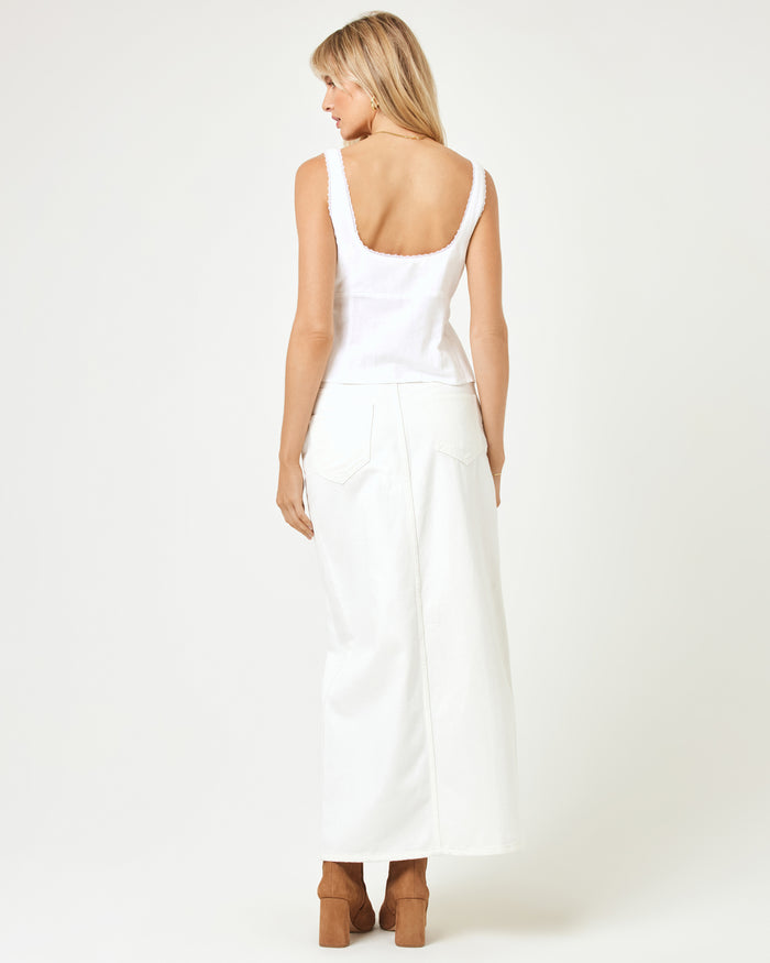 Back view of a model wearing the LSPACE Rosa Top in cream, showing the open back and frayed strap trim, styled with white wide-leg jeans and tan boots.