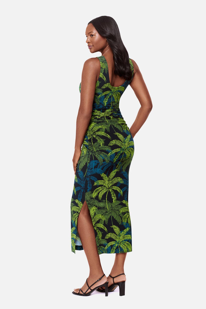 Woman turned left wearing a sleeveless full-length dress with a blue and green palm tree print
