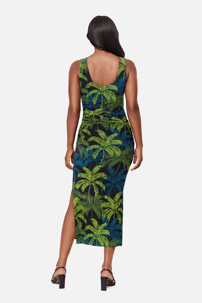 Woman turned away wearing a sleeveless full-length dress with a blue and green palm tree print
