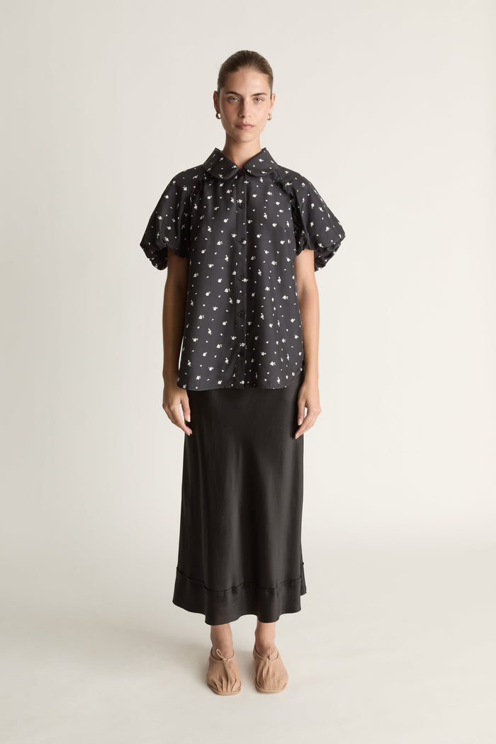 Woman wearing a black patterned blouse and black skirt on a white background