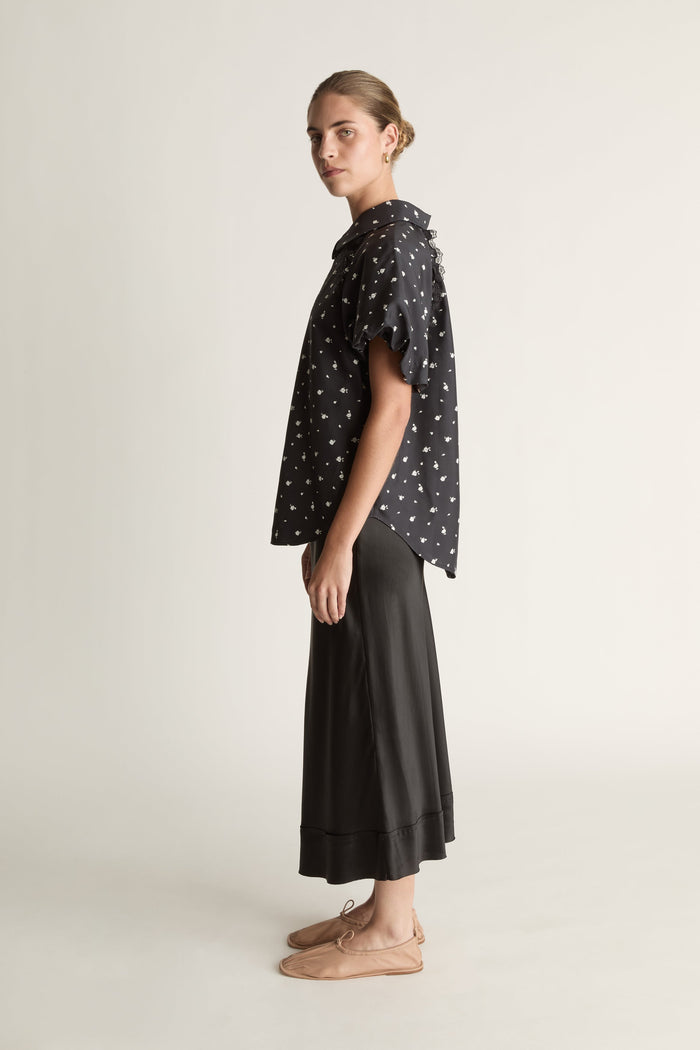 Woman wearing a black patterned blouse and black skirt on a white background