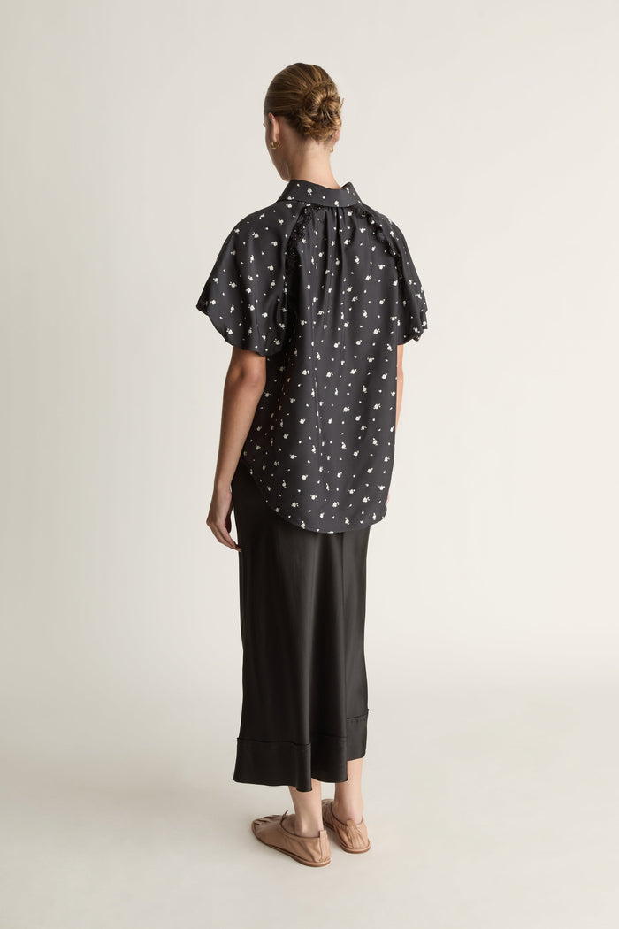Woman wearing a black patterned blouse and black skirt on a white background