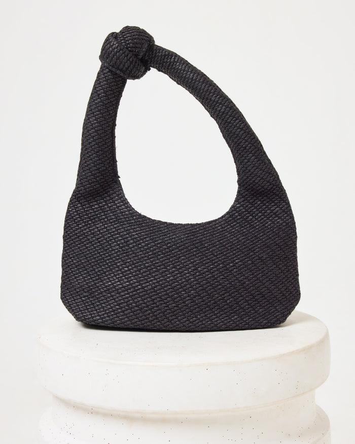 Off-model image of the Ryder Bag in black, a woven crescent hobo bag with a knotted handle, on a white pedestal.