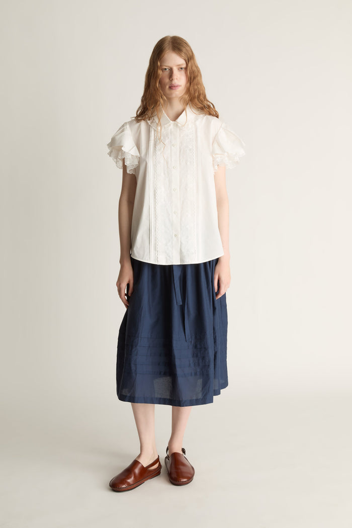 Woman wearing a white blouse and navy skirt on a plain background