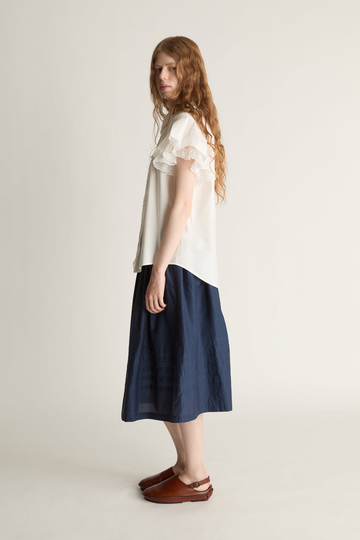 Woman wearing a white blouse and navy skirt on a plain background