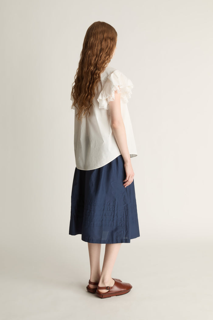 Woman wearing a white blouse and navy skirt on a plain background