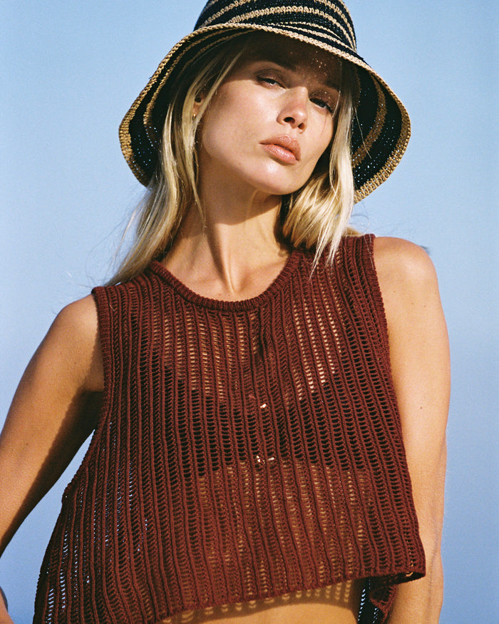 Close-up front view of a model wearing the LSPACE Sander Top in sangria, a sleeveless open-weave crochet crop top with a round neckline, styled with a striped bucket hat.
