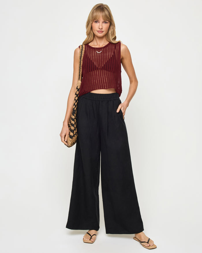 Front view of a model wearing the LSPACE Sander Top in sangria, a sleeveless open-weave crochet crop top styled with black wide-leg pants.