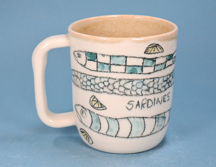 A ceramic mug with a handle, decorated with painted sardine illustrations, lemon slices, and the word 'SARDINES' in black lettering, set against a solid blue background.