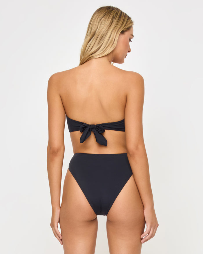 Back view of a model wearing the LSPACE after midnight hibiscus Savannah Bikini Bottom, showing the dark high-waist back, paired with a matching strapless bandeau Jasper Bikini Top with back tie closure.