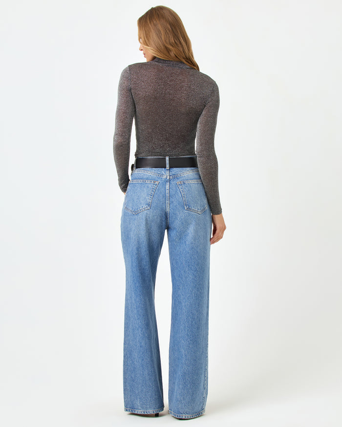 Back view of a model wearing the LSPACE Shimmer Long Sleeve in black, showing the sheer metallic sparkle fabric and fitted long-sleeve silhouette, styled with wide-leg jeans.