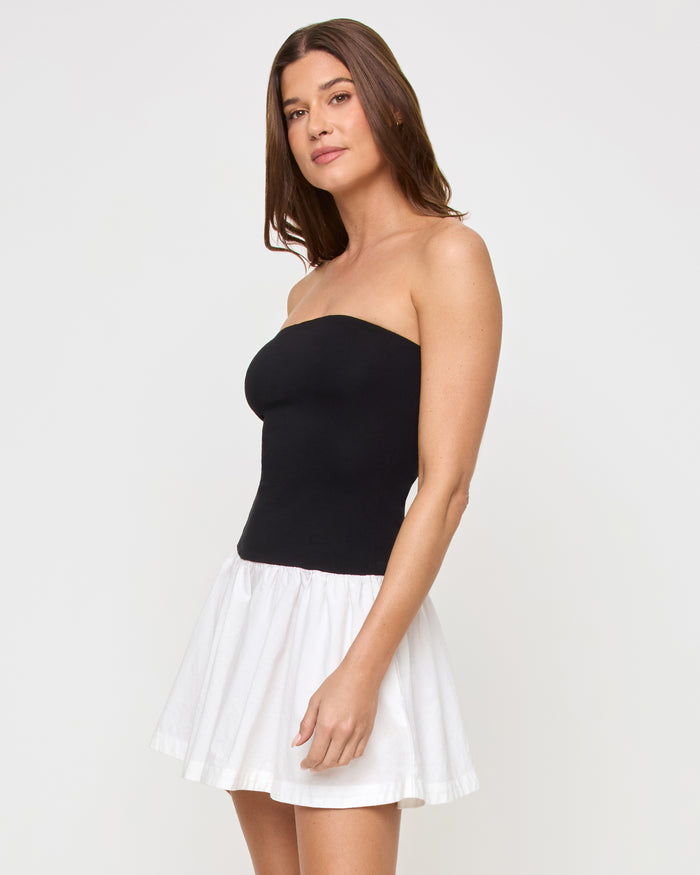 Side view of a model wearing the LSPACE Sienna Mini Dress in black-cream, highlighting the contrast between the fitted black strapless bodice and the voluminous cream ruffled skirt.