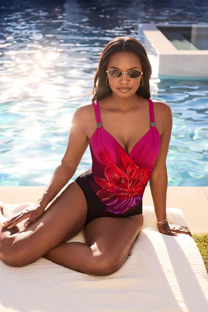 Woman on beach blanket wearing a red, pink and purple floral printed one-piece swimsuit