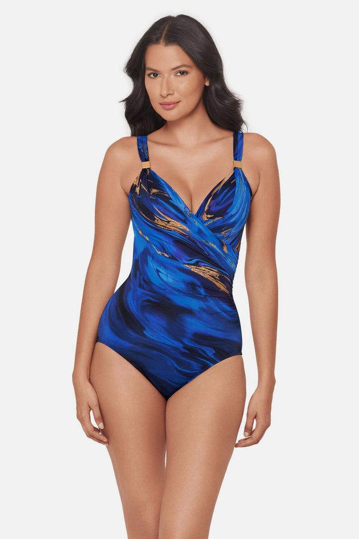 Woman wearing a blue and gold oil slick-esque printed one-piece swimsuit with strap details