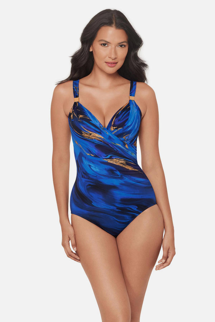 Woman wearing a blue and gold oil slick-esque printed one-piece swimsuit with strap details