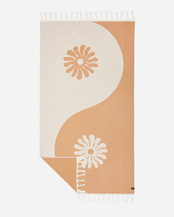 Flat lay of the Slowtide Botanic Balance Turkish Towel in brush, showing a yin-yang inspired pattern in warm tan and cream with daisy flower motifs and fringe detail.