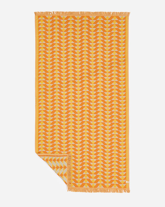 Flat lay of the Slowtide Daydream Driftweave Turkish Towel in curry, showing a golden orange geometric triangle pattern with fringe detail.