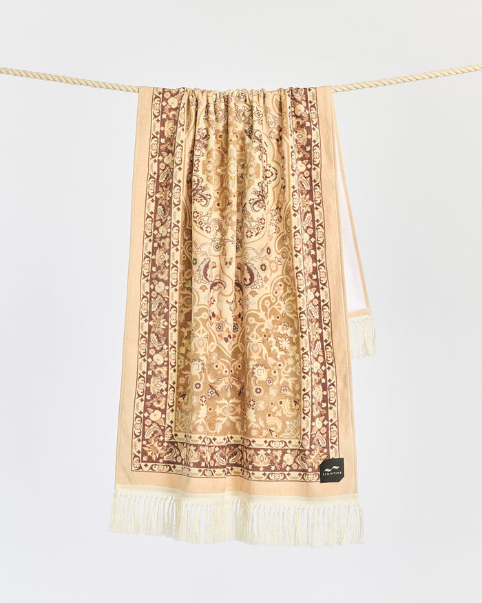 The Slowtide Haven Beach Towel in fawn hanging on a rope, displaying the Persian medallion pattern with fringe.