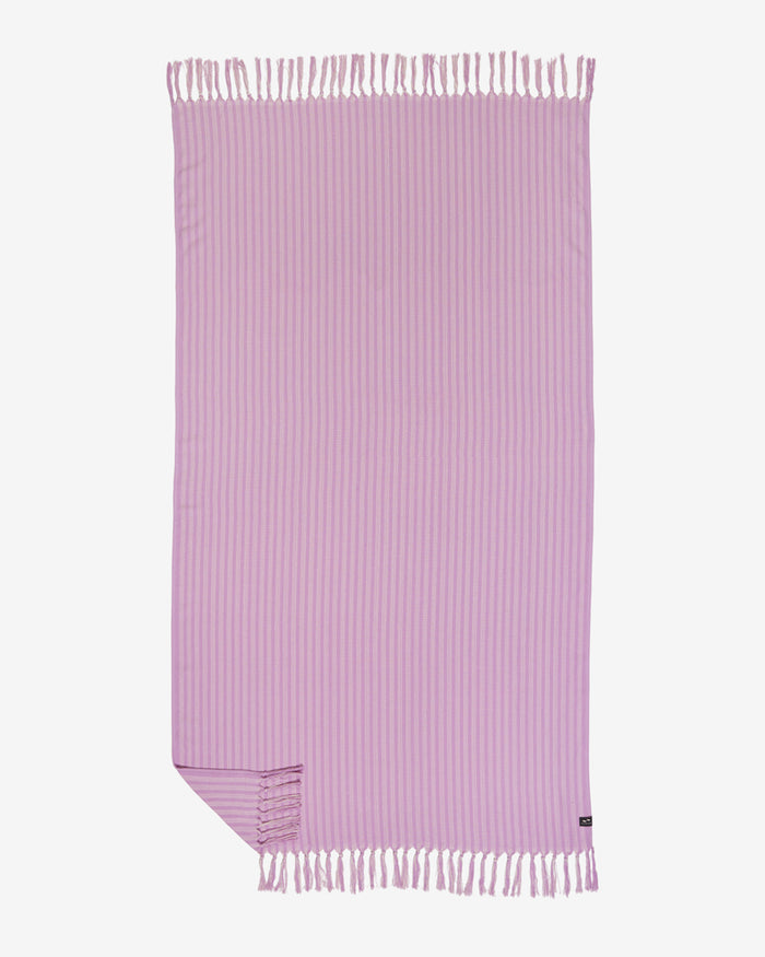 Flat lay of the Slowtide Koko Turkish Towel in ube, showing a solid lavender purple with fine vertical ribbed stripe texture and fringe on both ends.