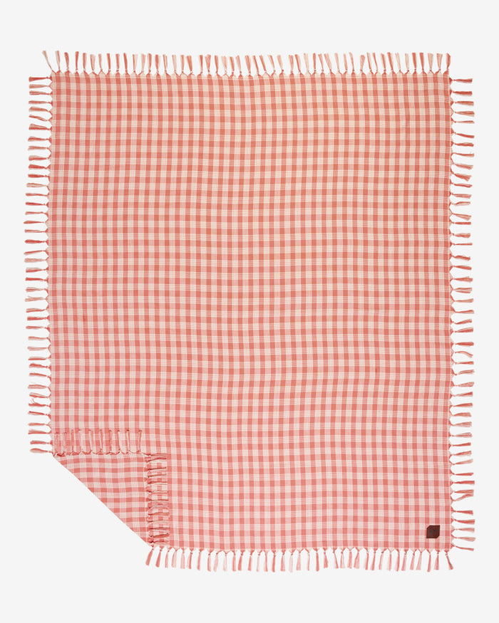 Flat lay of the Slowtide Palaka Lightweight Beach Blanket in guava, showing a pink gingham check pattern with fringe on all edges.