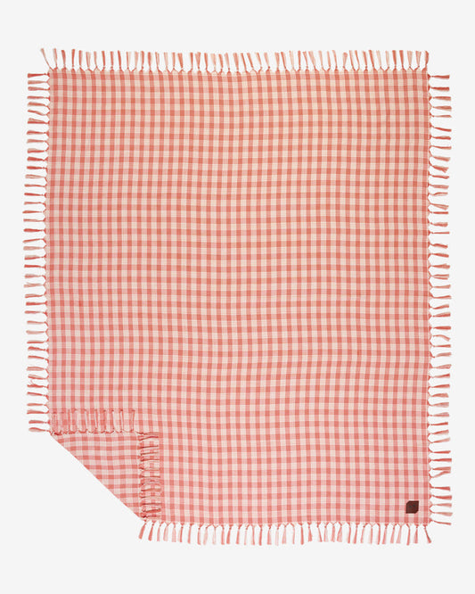 Flat lay of the Slowtide Palaka Lightweight Beach Blanket in guava, showing a pink gingham check pattern with fringe on all edges.